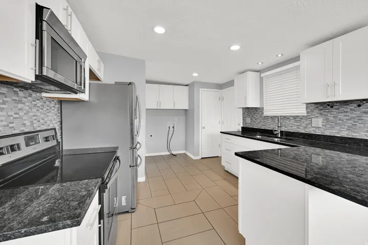 Kitchen featuring white cabinetry, dark stone countertops, and a mosaic tile backsplash
