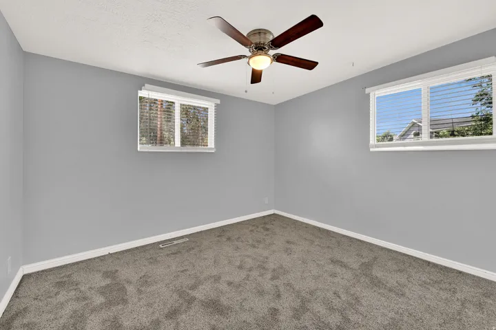 Carpeted room featuring a ceiling fan with integrated lighting, two windows with horizontal blinds, and baseboard trim