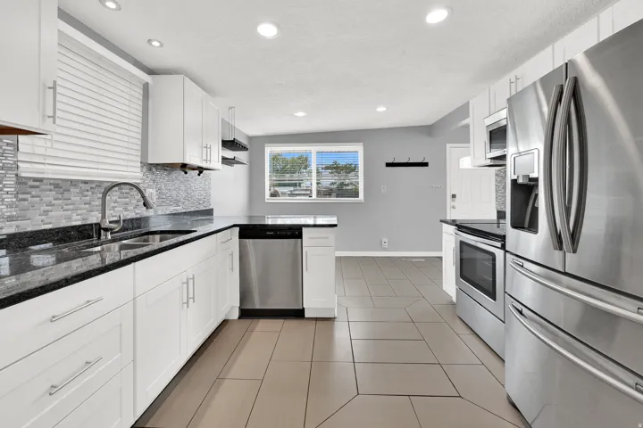 Kitchen featuring white cabinetry, dark countertops, a mosaic tile backsplash, stainless steel appliances, and large format floor tiling