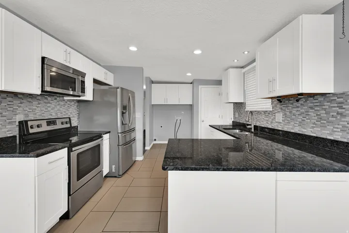 Kitchen featuring white cabinetry, dark stone countertops, stainless steel appliances, and a mosaic tile backsplash
