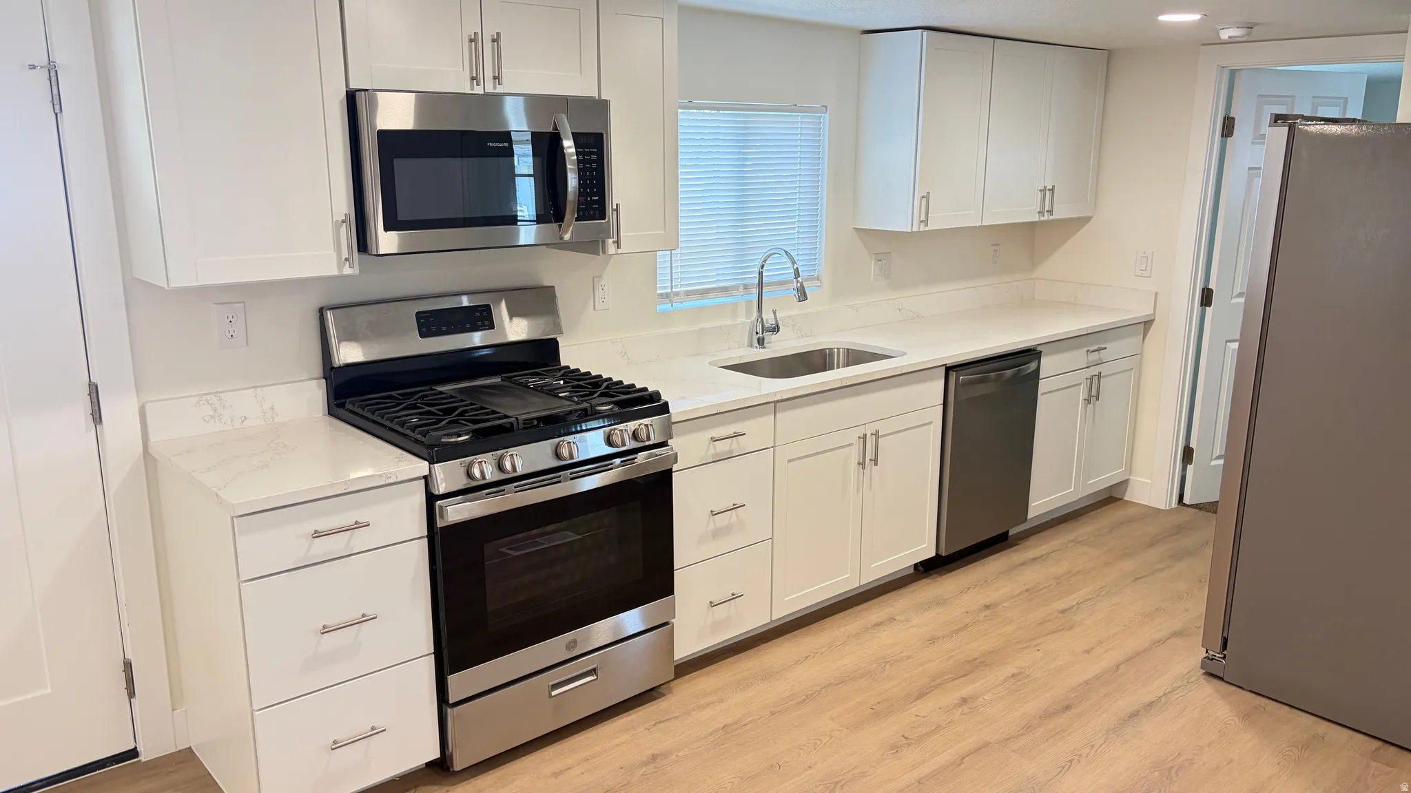 Kitchen featuring white shaker-style cabinetry, stainless steel appliances, light-colored countertops, and wood-finish flooring