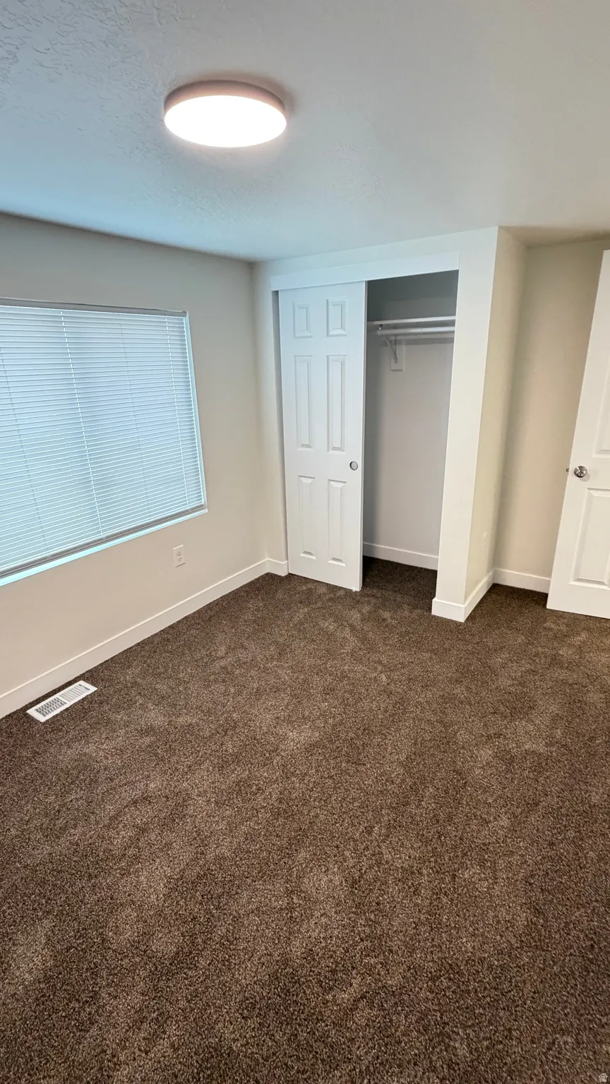 Carpeted room featuring a window with blinds, a sliding door closet with a hanging rod, a flush-mount ceiling light, and white baseboards