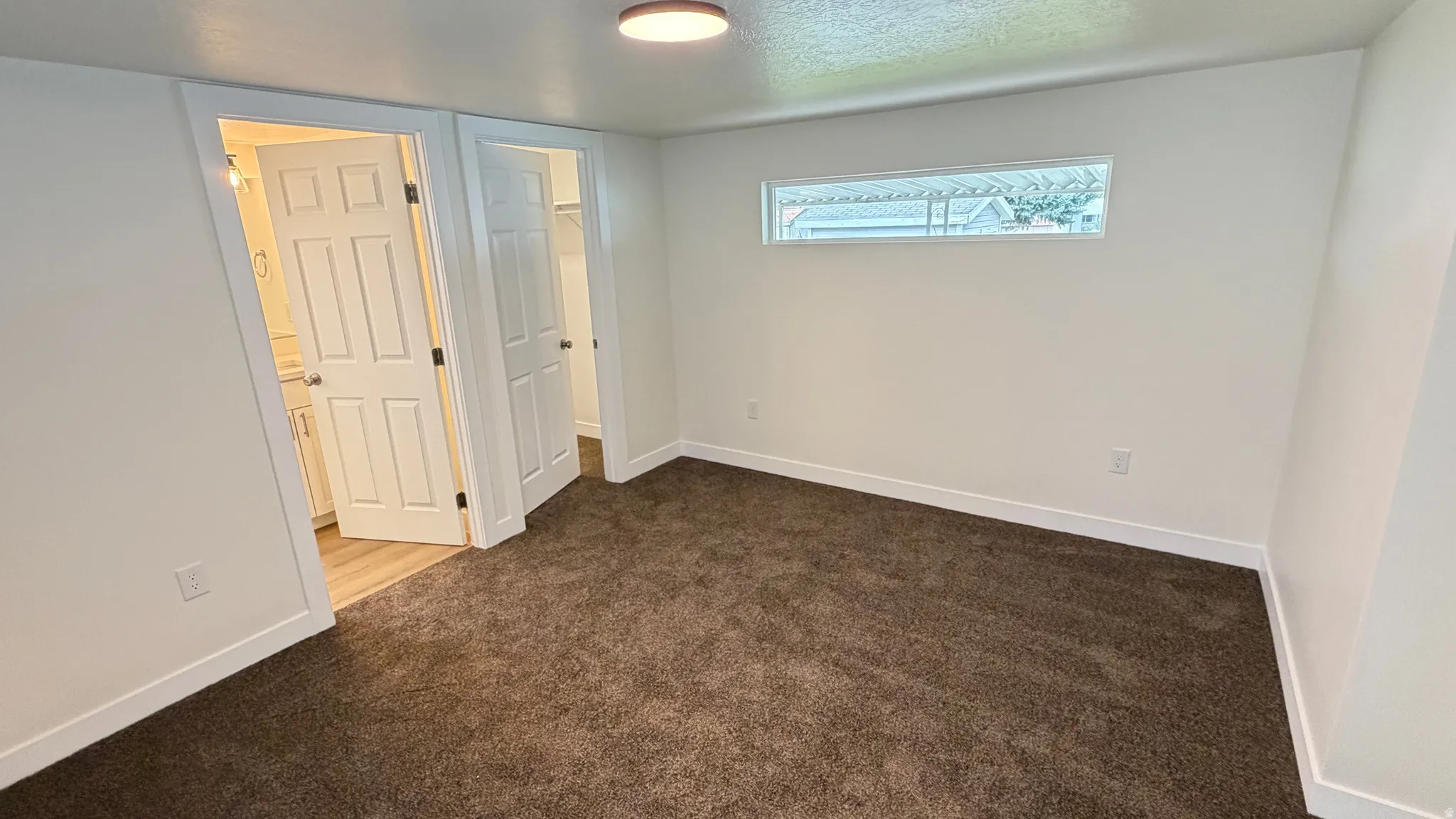 Neutral-toned wall-to-wall carpeting, white baseboards, and a horizontal transom window