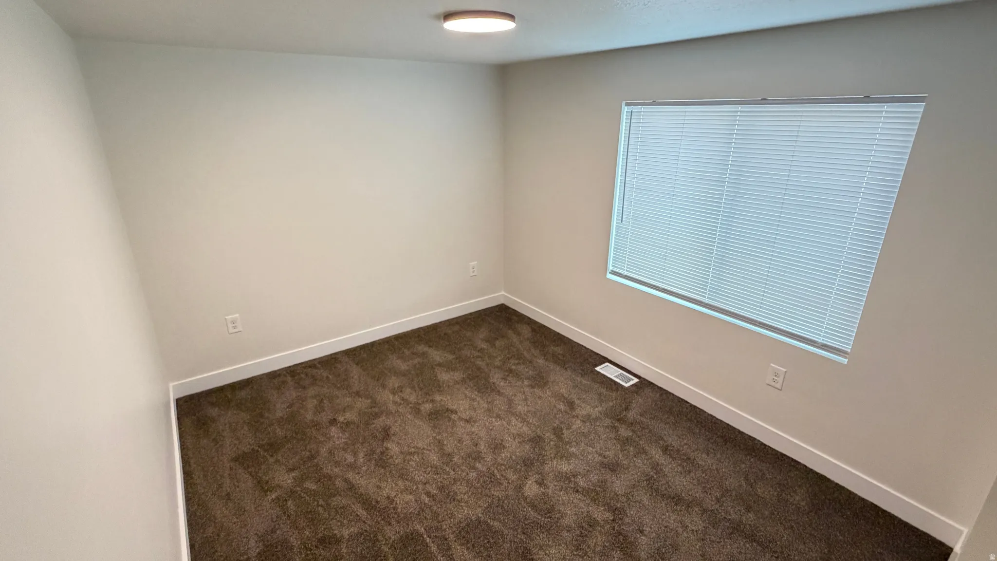 Carpeted room featuring a single window with horizontal blinds, neutral-toned walls, and white baseboards