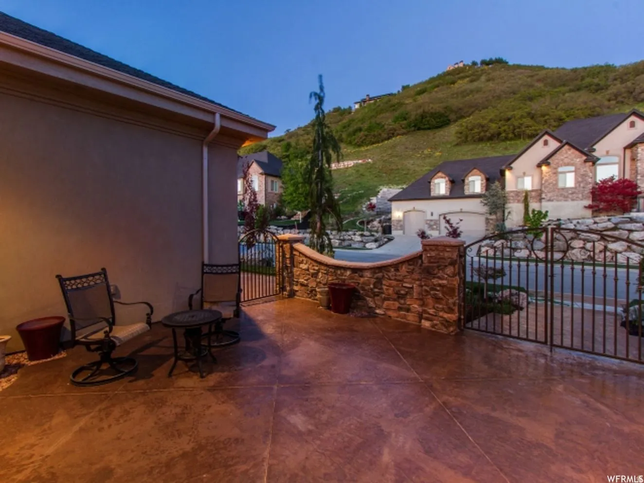 Stained concrete patio featuring a stone-clad retaining wall and wrought iron gate