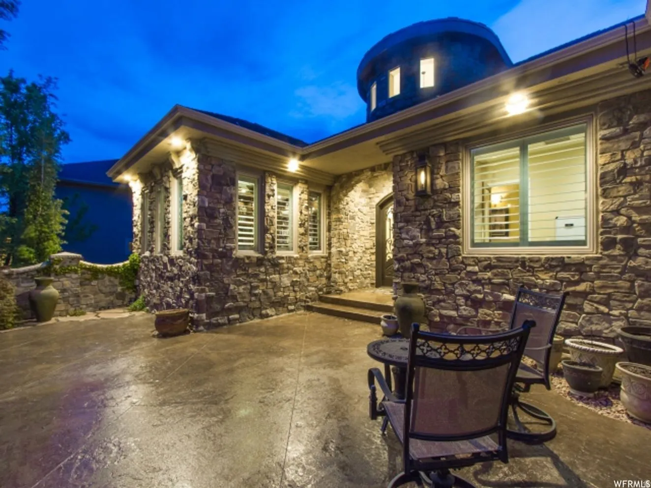Stone-clad exterior featuring multiple windows with interior plantation shutters, a decorative arched entry door, and exterior sconce lighting