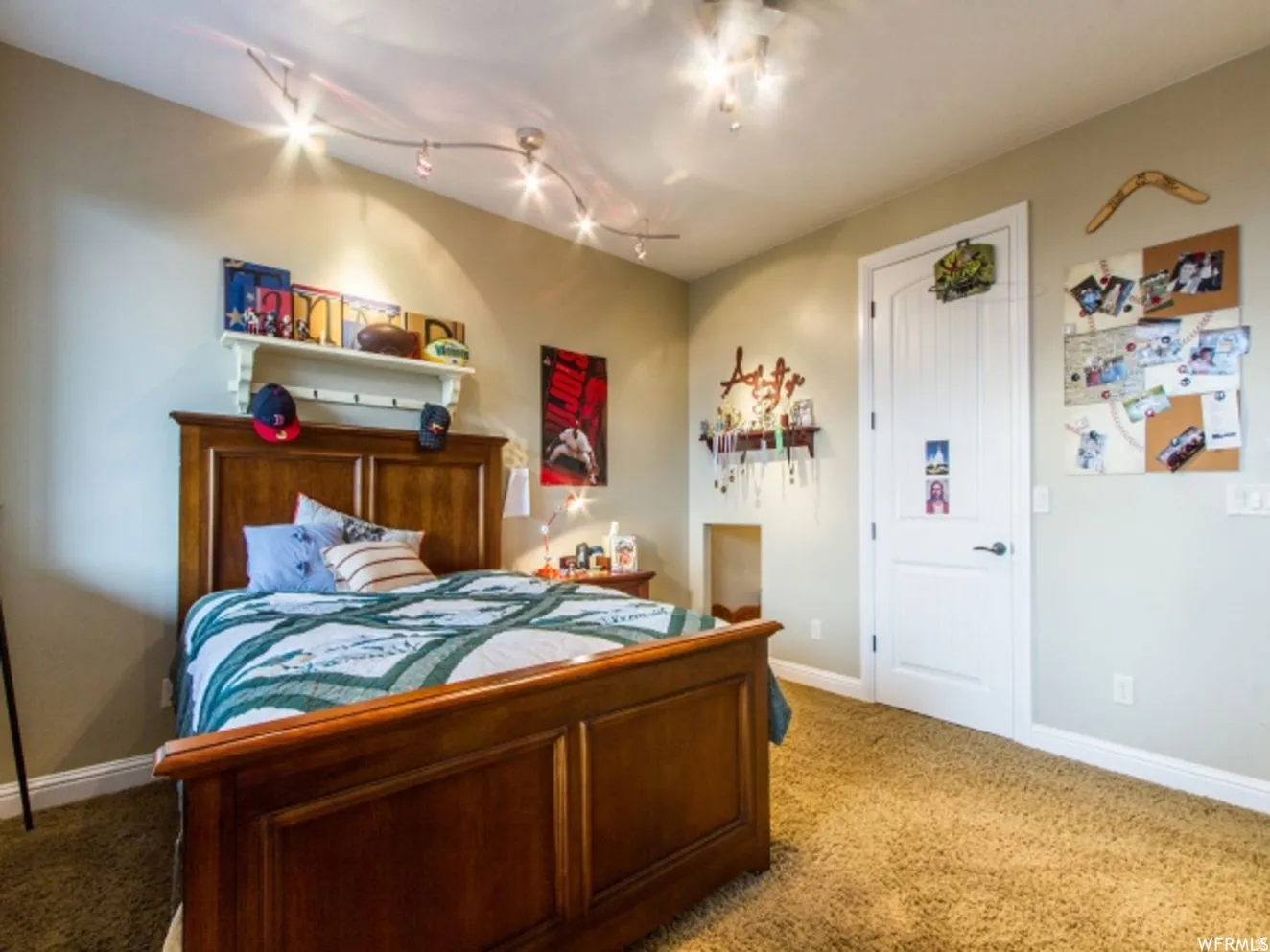 Warm bedroom featuring a wood-finish bed frame, track lighting, ceiling light fixture, neutral wall color, and textured carpet flooring
