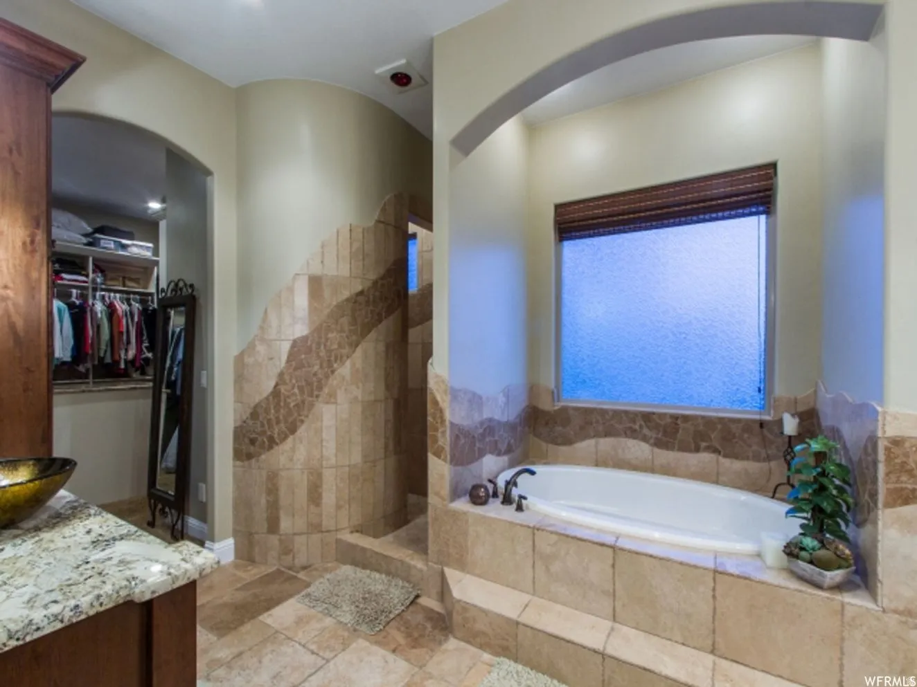 Spacious bathroom featuring a built-in soaking tub with surrounding tile, an arched alcove, and a frosted window with a woven shade