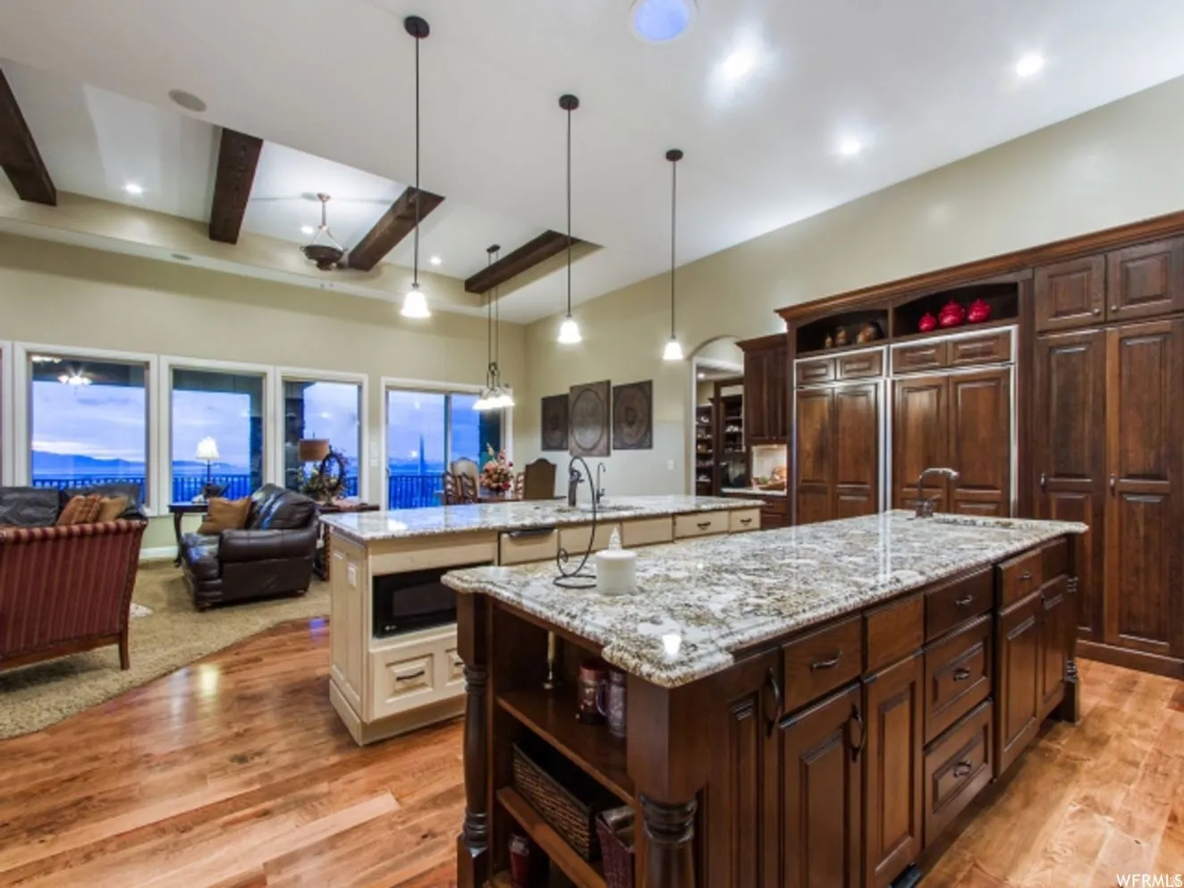 Open-concept kitchen and living area featuring dual islands with granite countertops, rich wood-finish flooring, and exposed ceiling beams