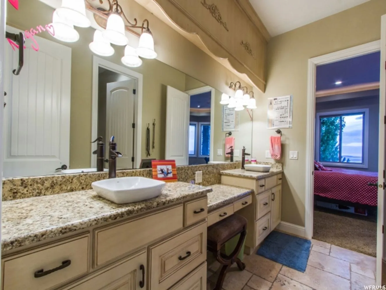 Bathroom vanity featuring dual vessel sinks, stone countertops, and cream-toned cabinetry with dark hardware