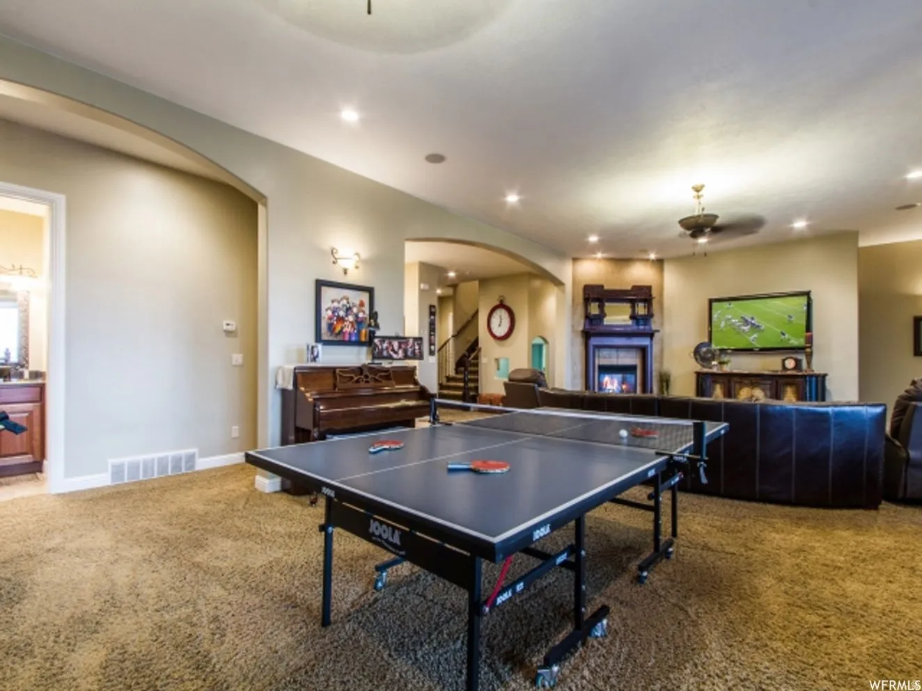 Spacious lower-level area with plush carpet flooring, recessed lighting, and an arched entryway