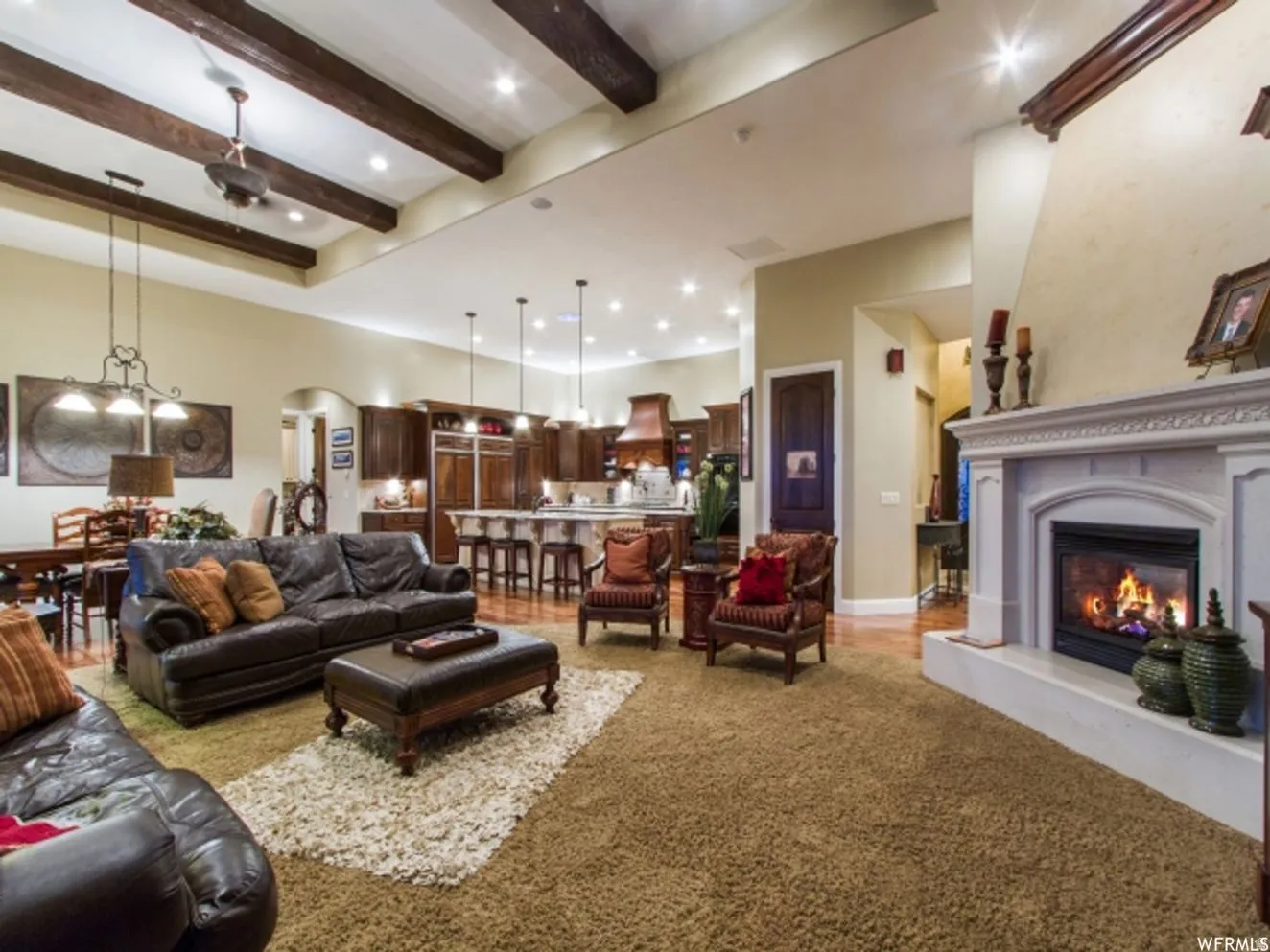 Spacious living area featuring a stone fireplace, wood-finish flooring, and exposed ceiling beams