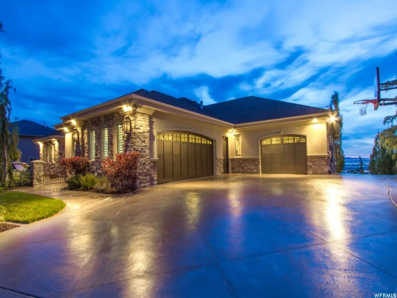 Stone and stucco exterior with multiple garage bays, exterior lighting, and a paved driveway