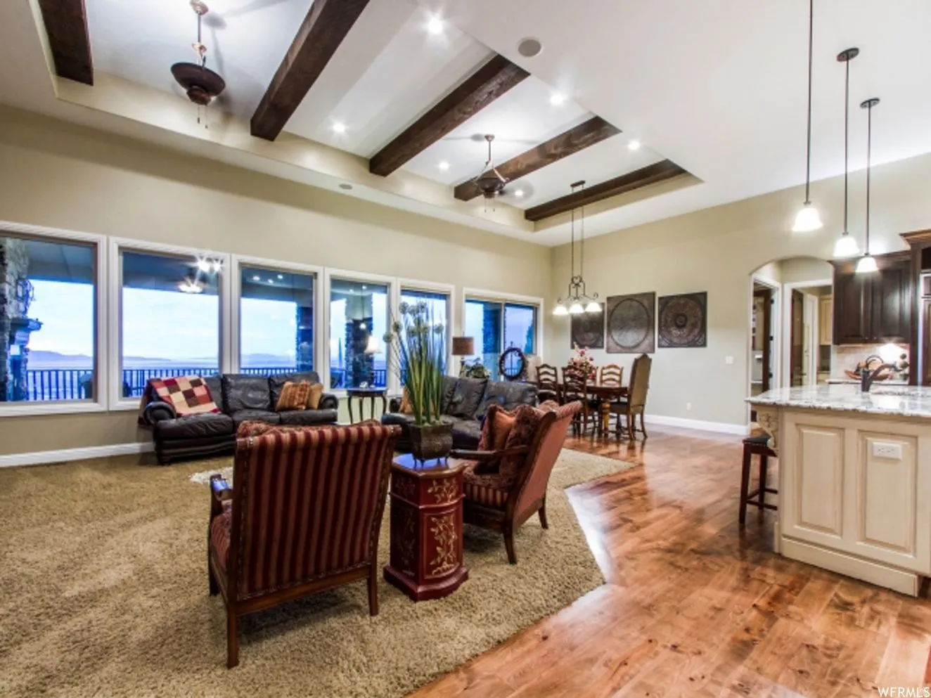 Spacious open concept living area featuring a tray ceiling with exposed wood beams, recessed lighting, and multiple windows