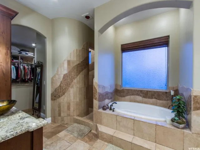 Spacious bathroom featuring a built-in soaking tub with surrounding tile, an arched alcove, and a frosted window with a woven shade