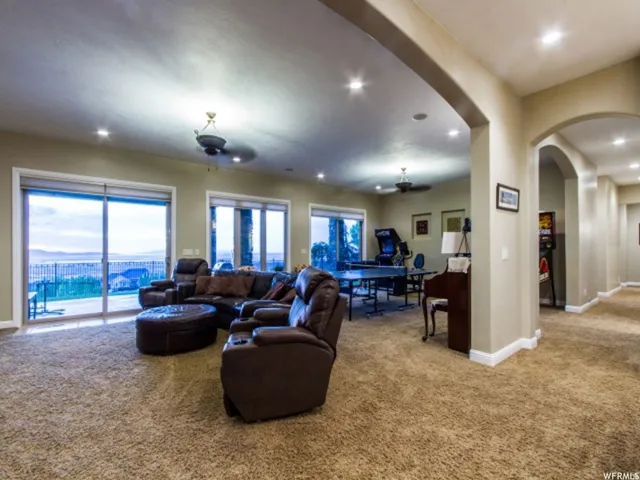 Spacious entertainment room featuring recessed lighting, plush carpet flooring, multiple sliding glass doors, ceiling fans, and a wide arched entryway