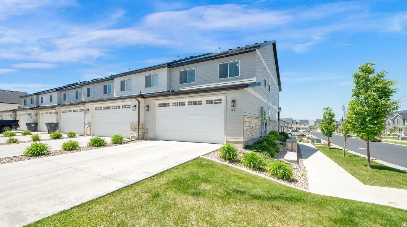 Modern townhome exterior featuring light gray siding, stone accents, white garage doors, and a concrete driveway