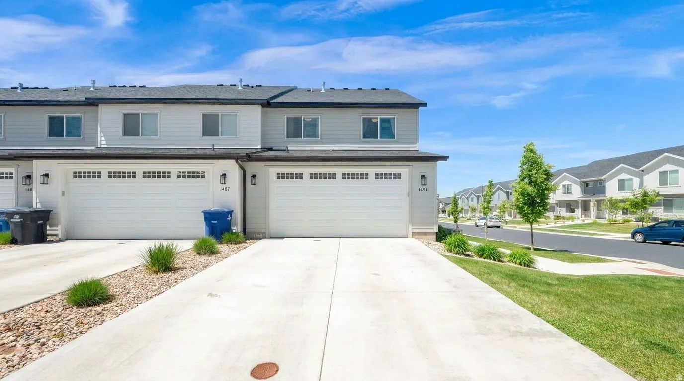 Modern townhome exterior featuring light gray siding, white garage doors, and a dark shingled roof