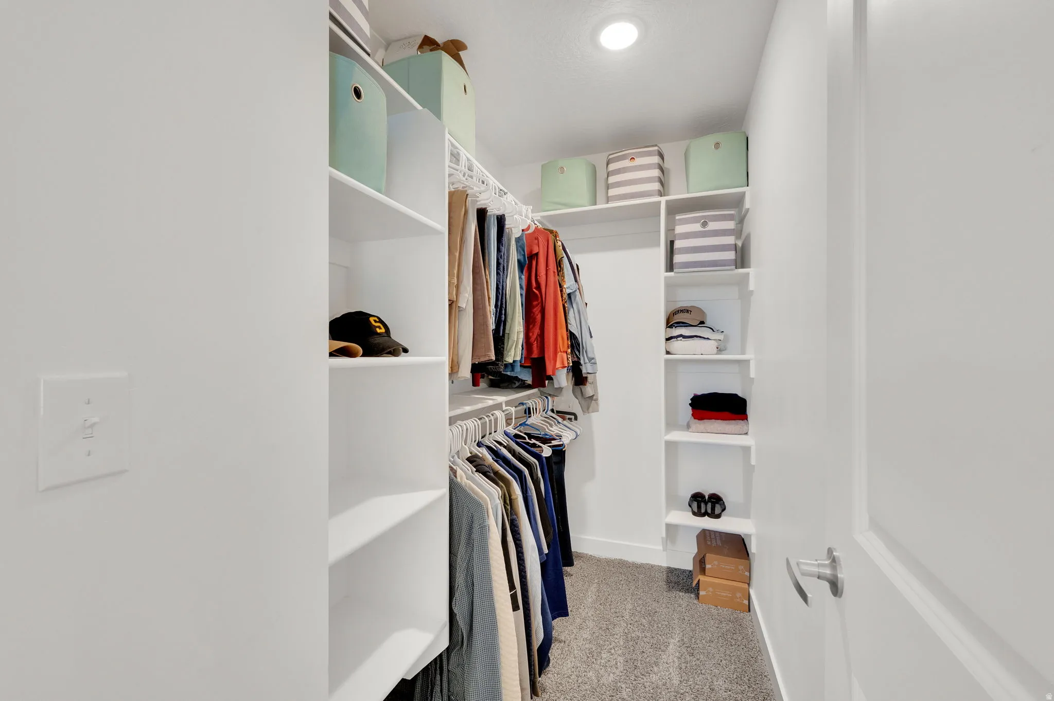 Walk-in closet featuring built-in white shelving, hanging rods, recessed lighting, and grey carpet flooring