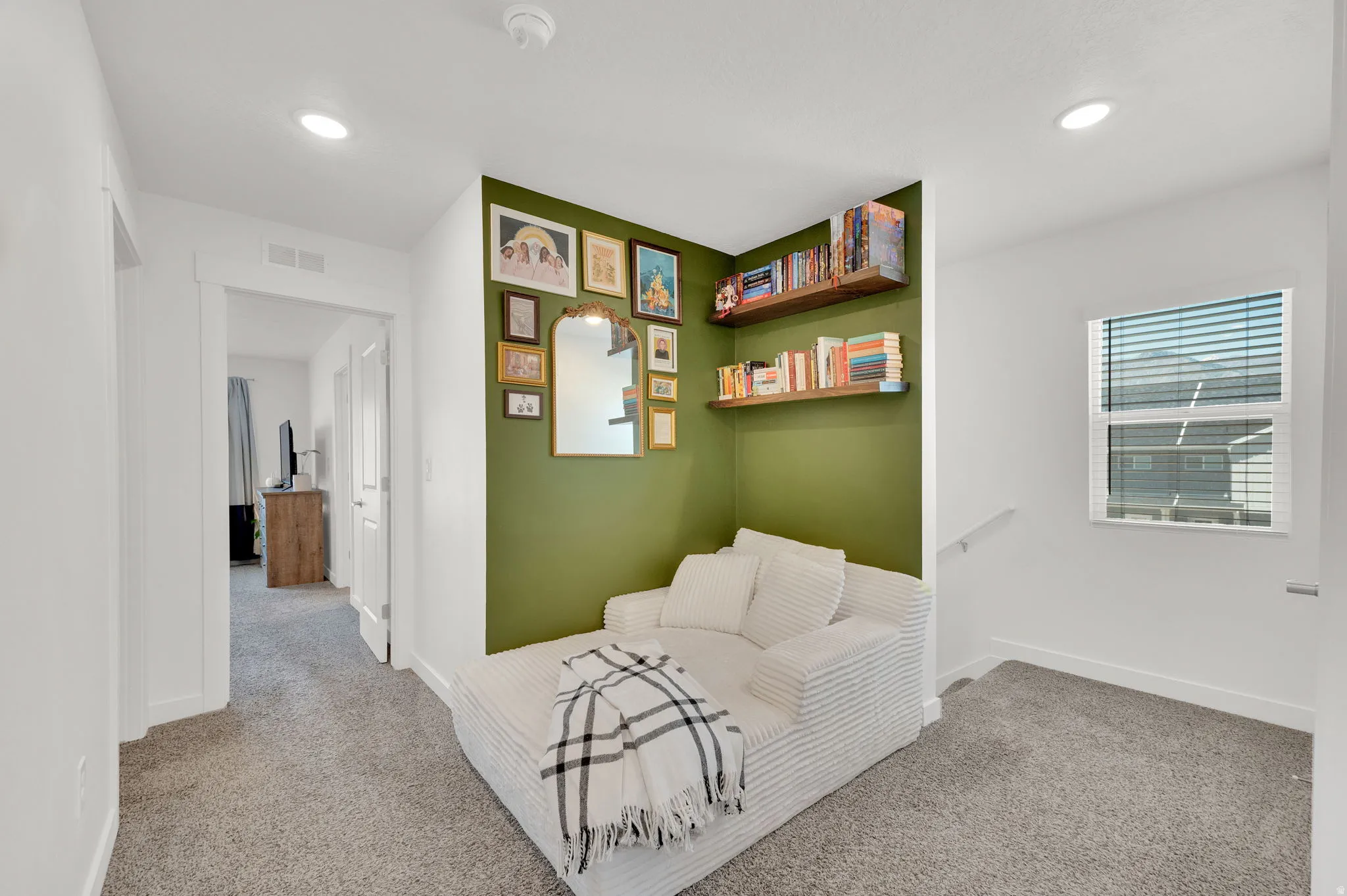 Dedicated reading nook with accent wall, recessed lighting, two wood-finish floating shelves, light gray carpeting, and white baseboards