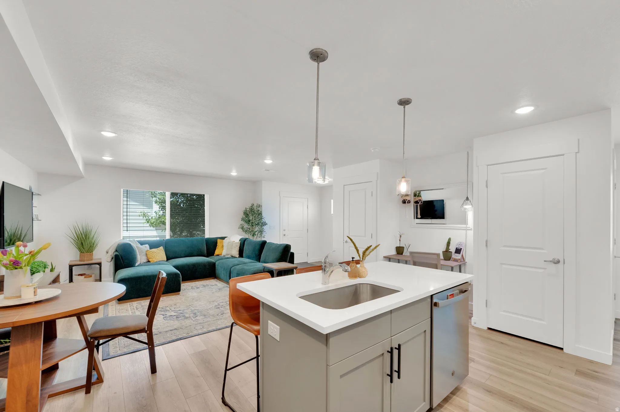 Open-concept living space featuring wood-finish flooring, recessed lighting, and a kitchen island with an undermount sink and pendant lighting
