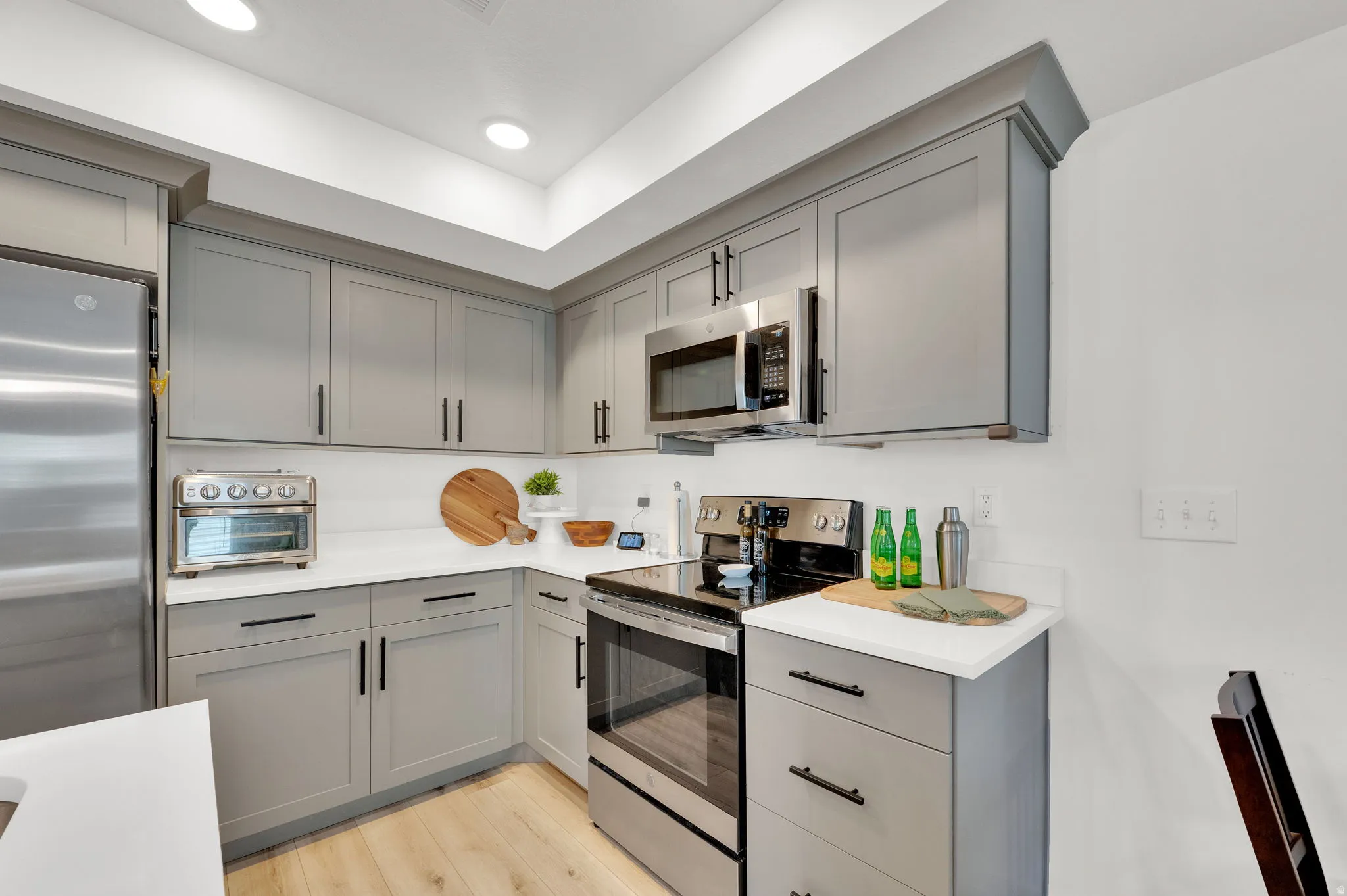 Contemporary kitchen featuring light gray cabinetry, stainless steel appliances, white countertops, and wood-finish flooring