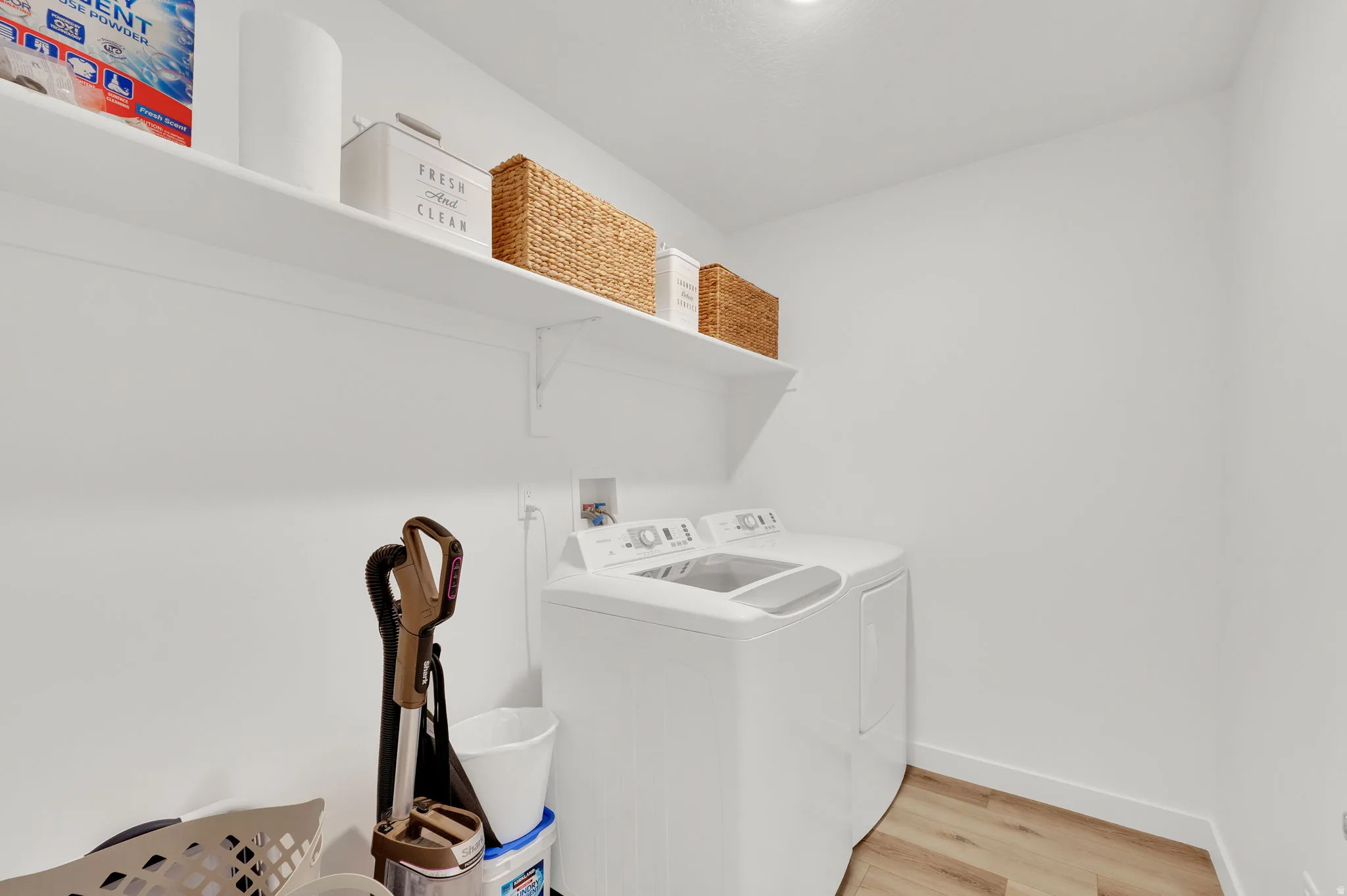 Dedicated laundry area featuring a white top-load washer, wood-finish flooring, and white walls