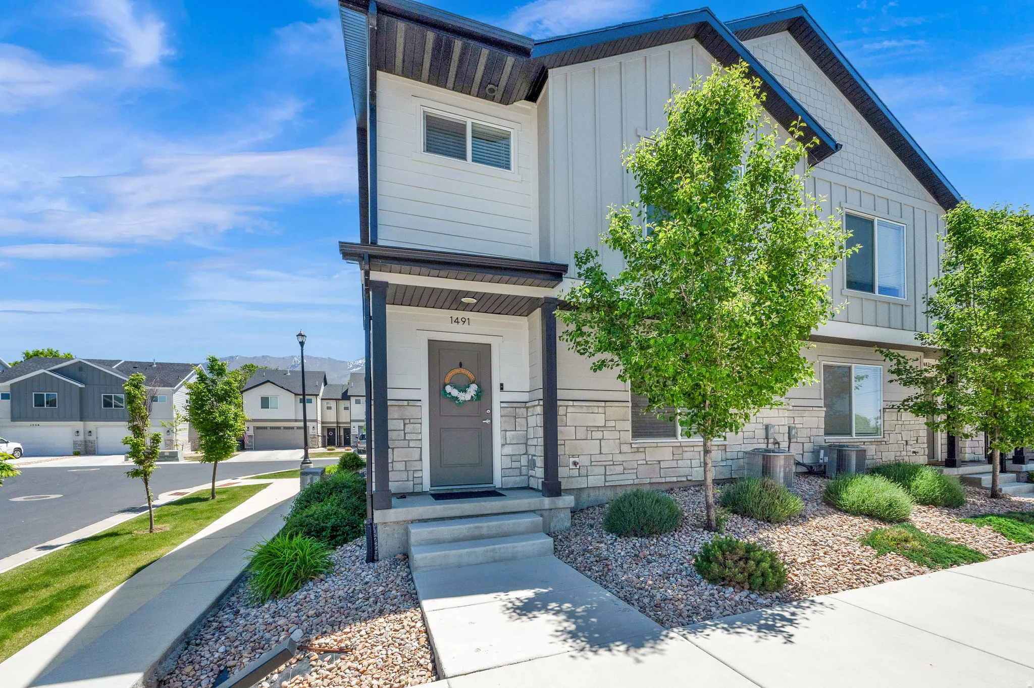 Modern townhome exterior featuring light-colored siding, a stone facade, and dark trim accents