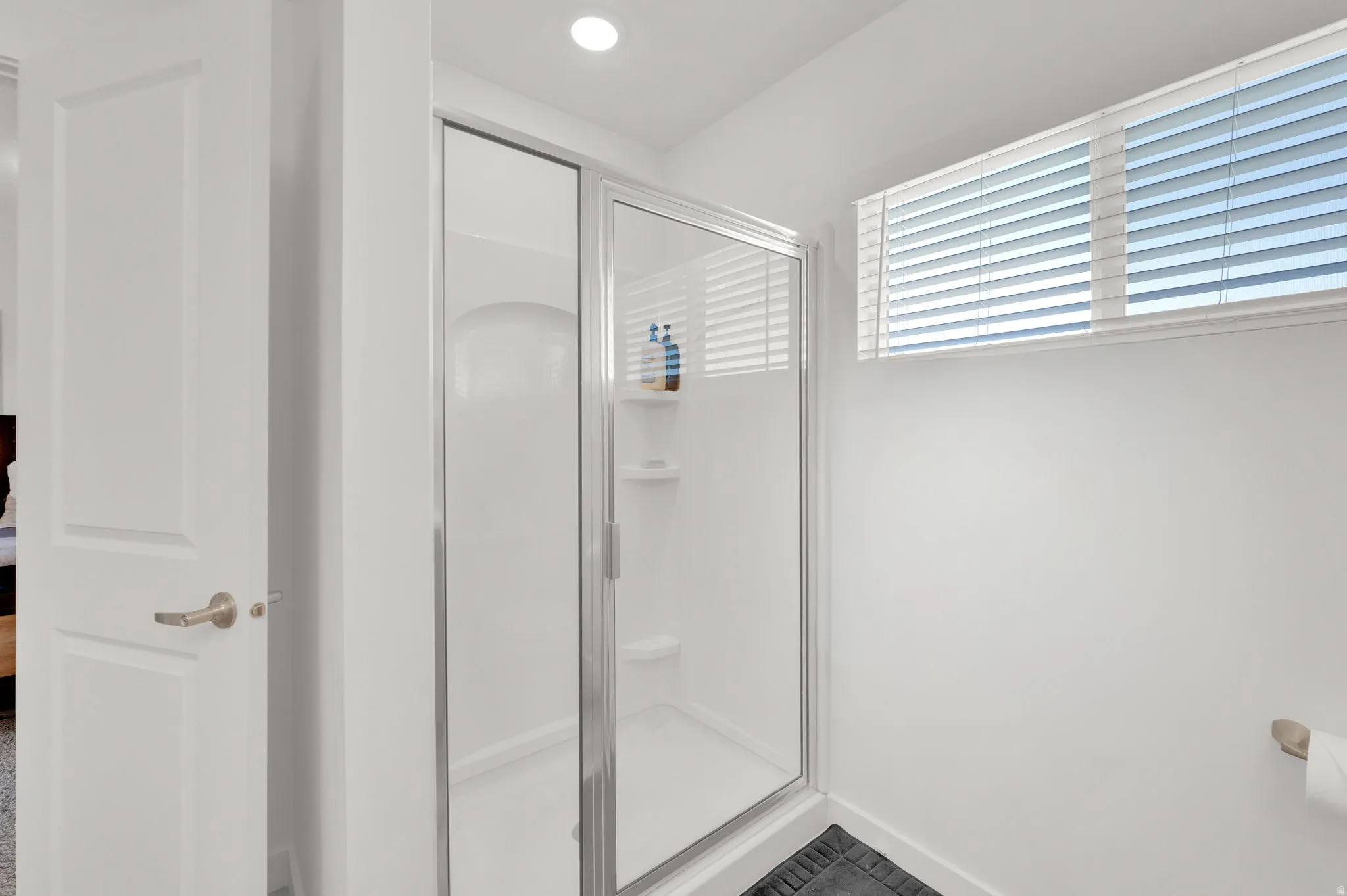 Shower enclosure with clear glass door, white surround, and integrated shelving