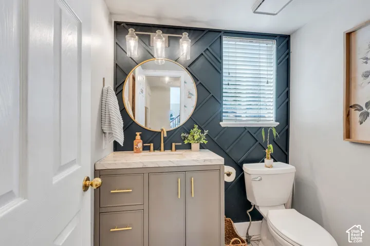 Powder room featuring a patterned accent wall, single vanity with a stone countertop, under-mount sink, and a circular mirror