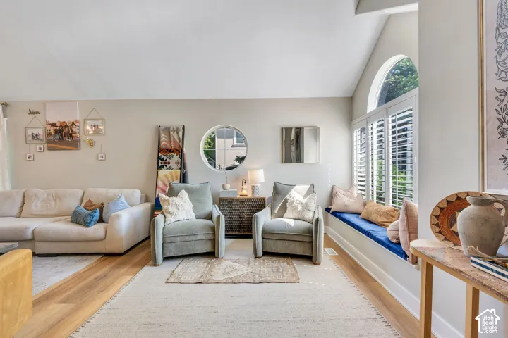 Vaulted ceiling living area featuring wood-finish flooring, a built-in window seat with plantation shutters, and an arched window