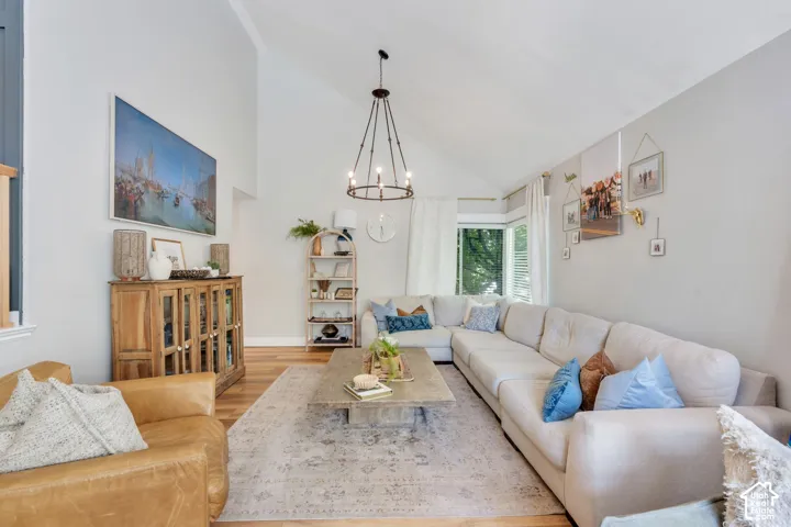 Vaulted ceiling living area featuring wood-finish flooring, a contemporary chandelier, and a bay window