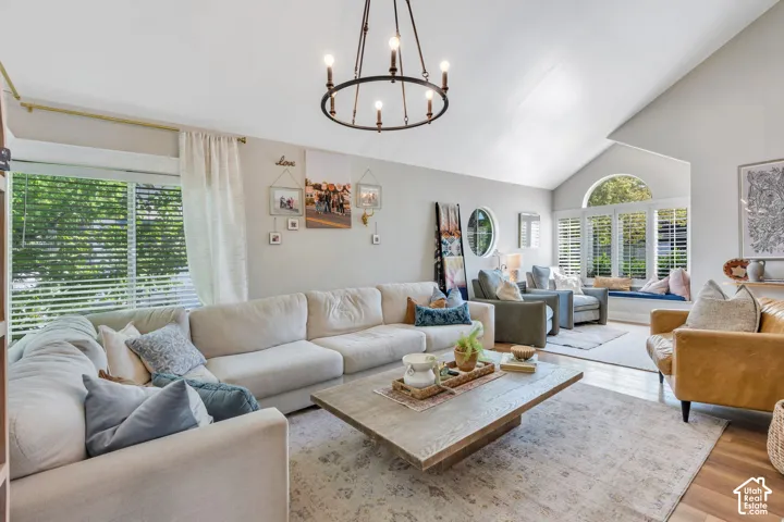 Vaulted ceilings enhance this living space featuring a dark bronze chandelier, large windows with horizontal blinds, and light wood-finish flooring