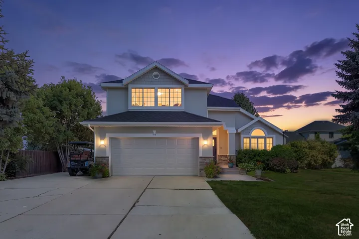 Two-story residence featuring a stucco and stone veneer exterior, a two-car garage, and established landscaping