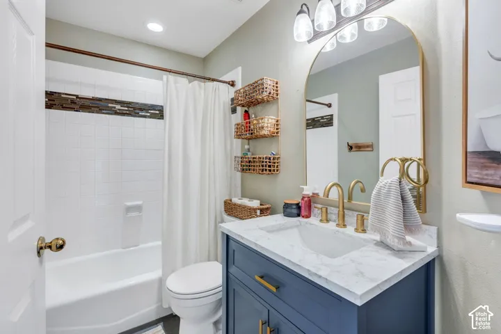 Bathroom featuring a white subway tile shower with a decorative mosaic accent, a vanity with a white countertop and rectangular undermount sink, a gold-framed arched mirror, and a three-light vanity fixture