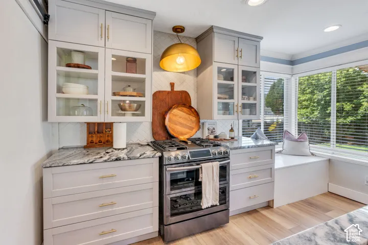 Kitchen featuring light gray cabinetry with gold hardware, a built-in window seat, stainless steel range, patterned tile backsplash, and light wood-finish flooring
