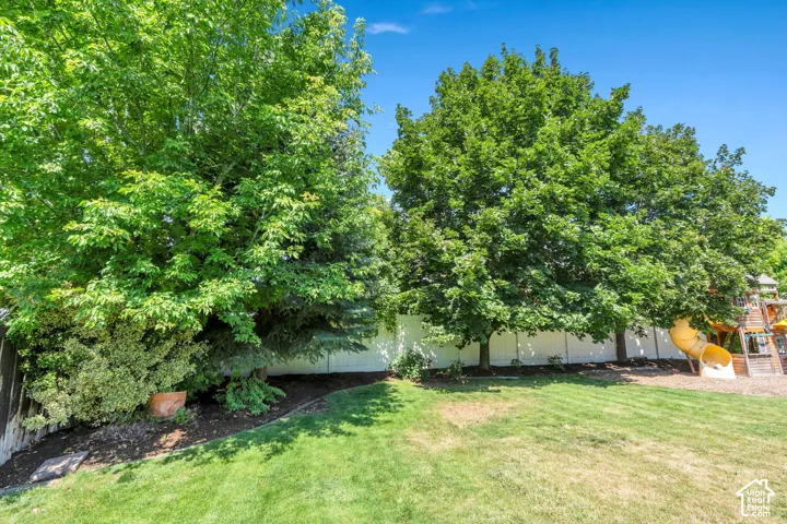 Expansive backyard featuring a manicured lawn, mature shade trees, and a white privacy fence