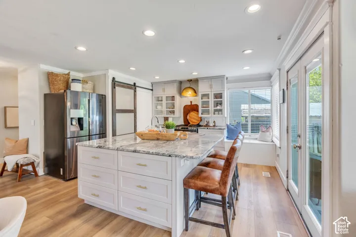 Kitchen featuring an expansive central island with stone countertop and integrated storage, light wood-finish flooring, recessed lighting, and a window seat