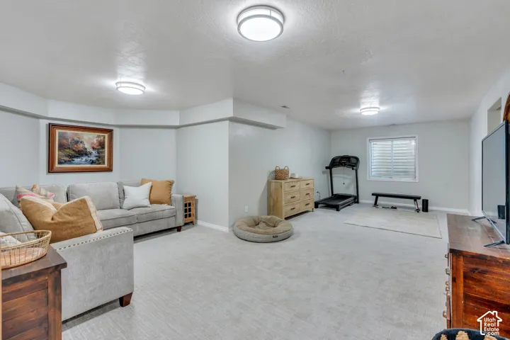 Spacious lower-level room featuring light gray carpeting, recessed ceiling lighting, and a window with horizontal blinds