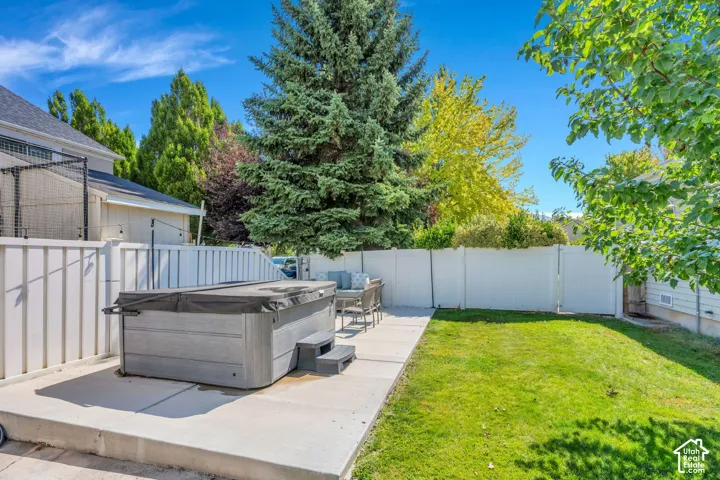 Expansive backyard featuring a built-in hot tub, concrete patio, and a privacy fence