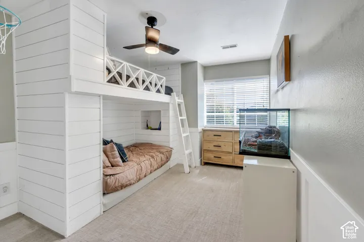 Built-in bunk bed structure with shiplap-style paneling, integrated ladder, ceiling fan with light fixture, window with blinds, and light-toned carpeting