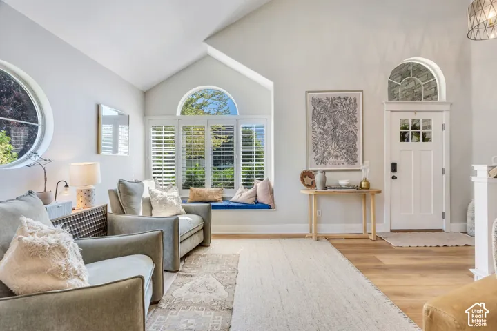 Vaulted ceiling living space featuring a window seat with plantation shutters, large circular window, and wood-finish flooring