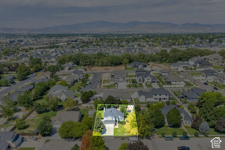 Aerial perspective showcasing a residential property with a light-colored exterior and a dark roof, surrounded by mature trees