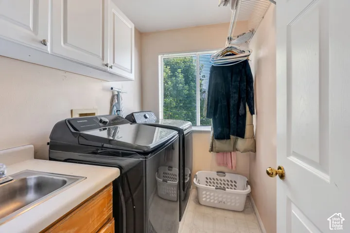 Dedicated laundry area featuring a utility sink, white upper cabinetry, and a window for natural light