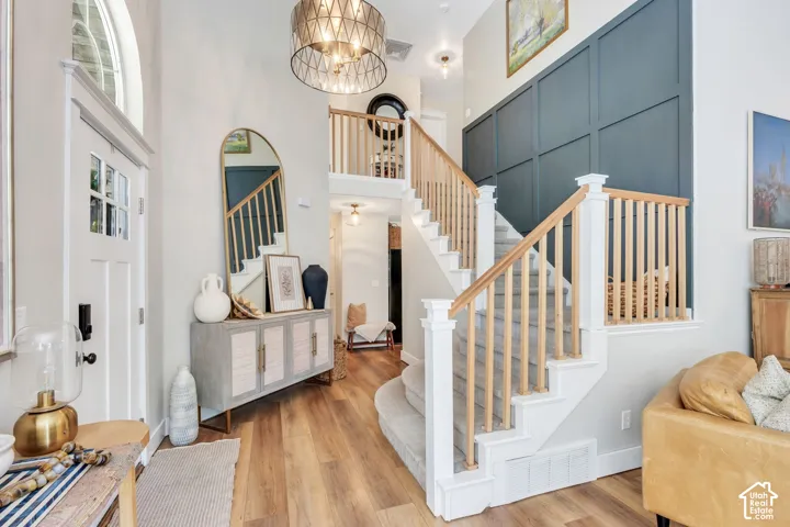Two-story entryway featuring wood-finish flooring, a contemporary chandelier, board and batten accent wall, a staircase with wood railings, and a transom window above the entry door