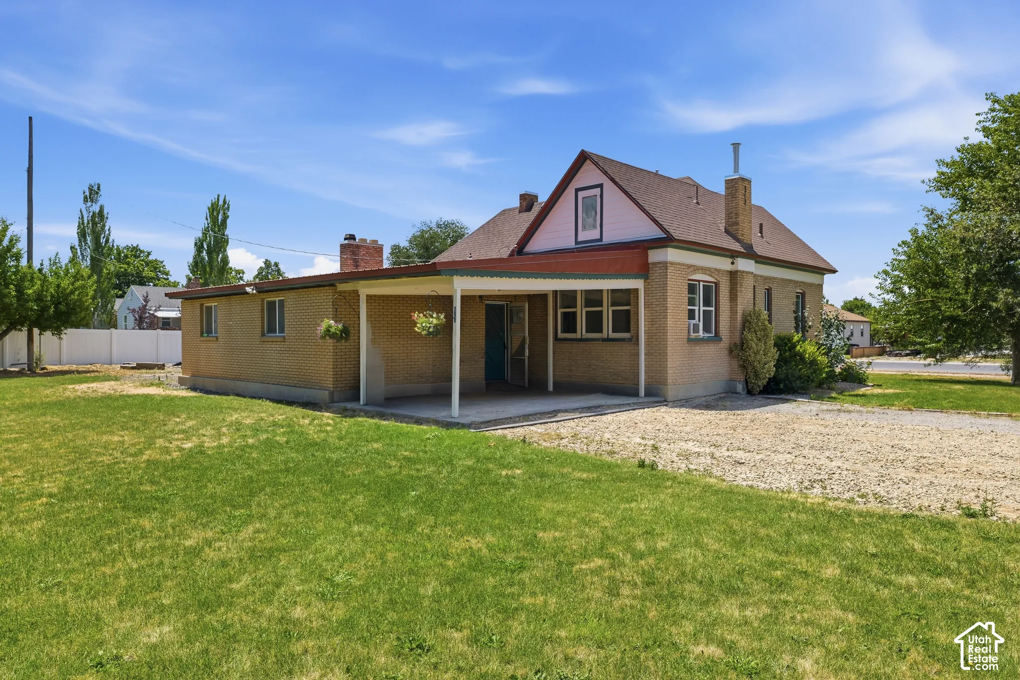 Brick exterior with a covered patio, a gravel driveway, and a spacious lawn