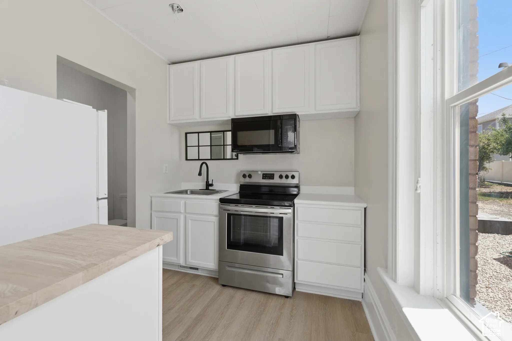 Kitchen featuring white cabinetry, stainless steel range and microwave, light wood-finish flooring, and a white countertop with an undermount sink and matte black faucet