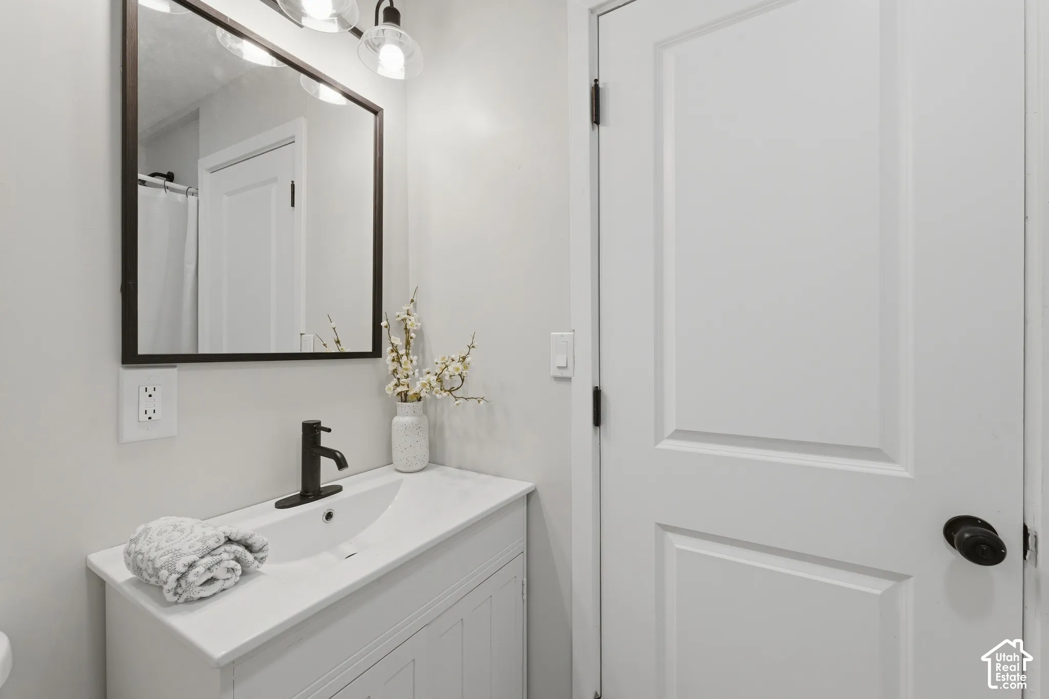 White vanity with an integrated sink and matte black faucet, complemented by a rectangular framed mirror and three-light vanity fixture