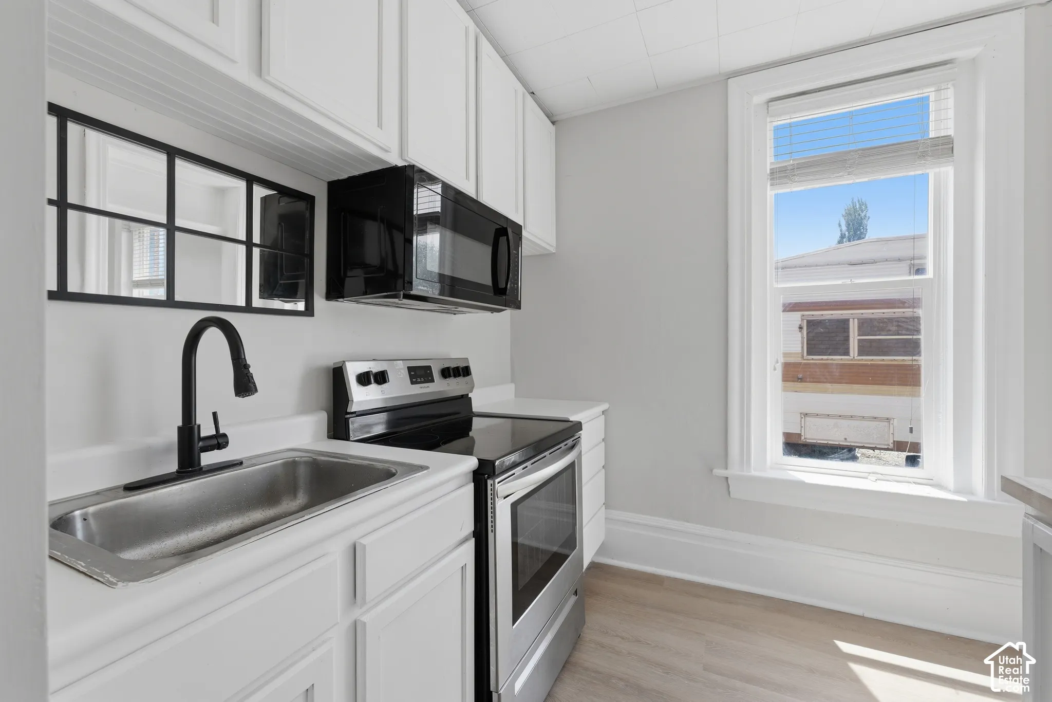 Galley kitchen featuring white cabinetry, stainless steel sink with matte black faucet, stainless steel electric range, built-in microwave, and wood-finish flooring