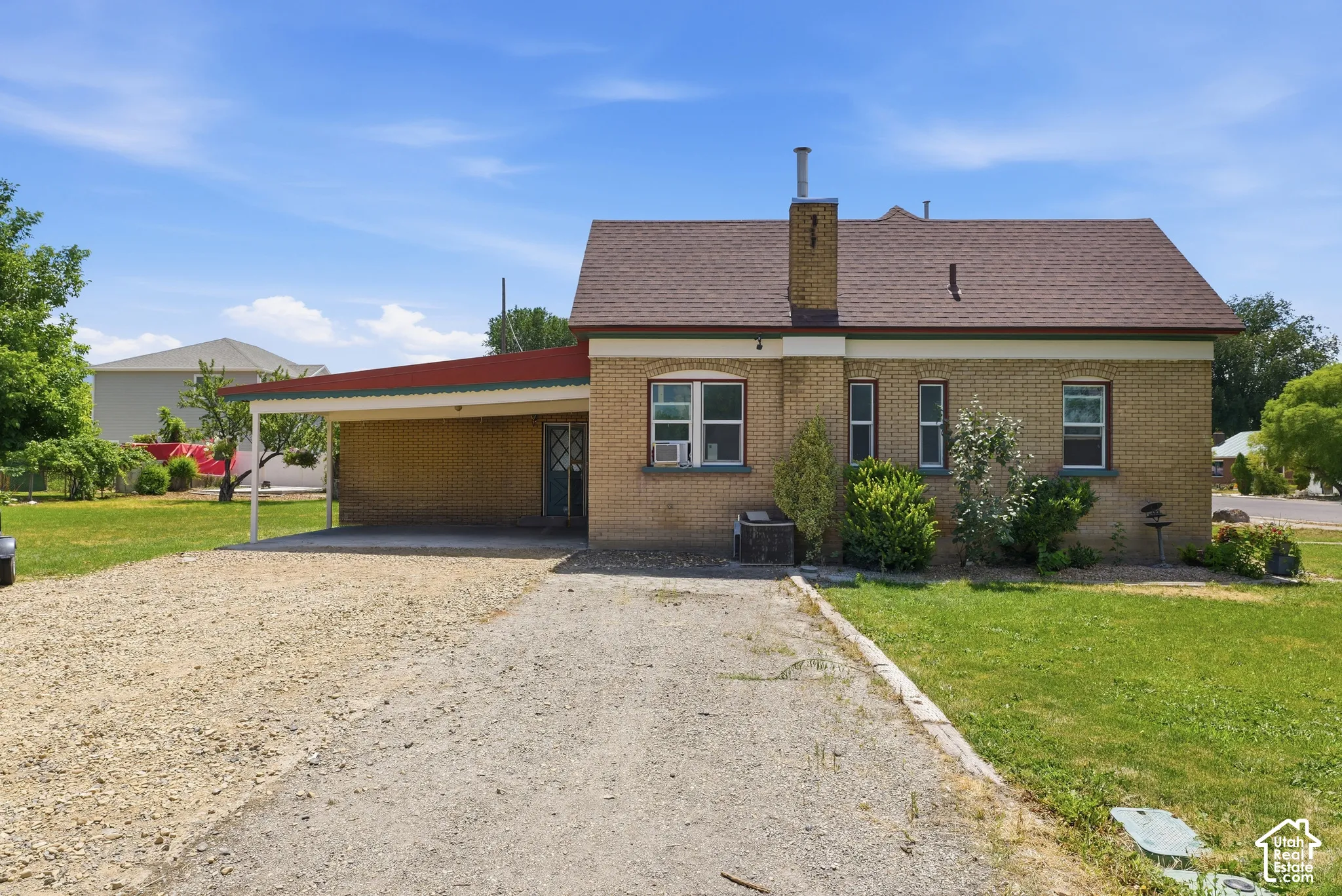 Brick exterior featuring a covered carport, pitched roof, and a gravel driveway